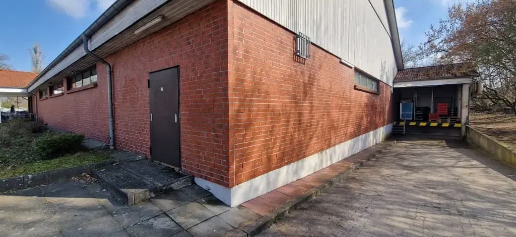 Ceglana ściana za sklepem po usunięciu graffiti — czysta cegła i odświeżony cokół